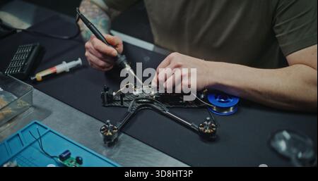 Nahaufnahme eines Ingenieurs, der an kundenspezifischen elektronischen Lösungen für die Drohnenplattform arbeitet. Mann Löten empfindlicher Drähte an kleinen Drohnen Controller. Problemlösung und Innovation, die in Drone RD und Design inhärent sind. Stockfoto