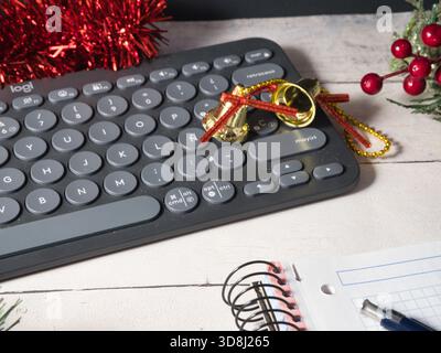 Weihnachtstastatur Holiday Workspace – Nahaufnahme einer Tastatur mit festlicher Weihnachtsdekoration, einschließlich rotem Lametta, goldenen Glocken und Berr Stockfoto