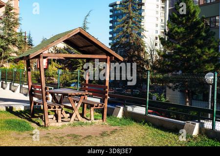 Hölzerner Pavillon mit Picknicktisch und Bänken auf Gras in einem Stadtpark, umgeben von Bäumen und Wohngebäuden Stockfoto