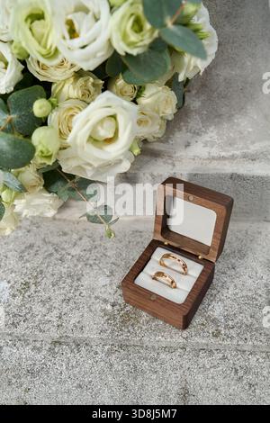 Hochzeitsringe in Holzkiste mit weißem Rosenstrauß. Stockfoto