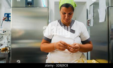 Die Hände des Küchenchefs kneten und Formen gelben Pasta-Teig auf einer rustikalen Holzoberfläche und zeigen den akribischen Prozess der handgemachten Zubereitung von Speisen in a b Stockfoto