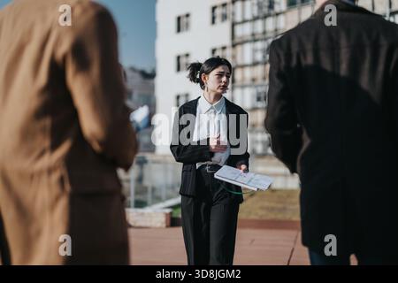 Eine professionelle Frau leitet ein Geschäftstreffen im Freien auf dem Dach und präsentiert den Kollegen Dokumente Stockfoto