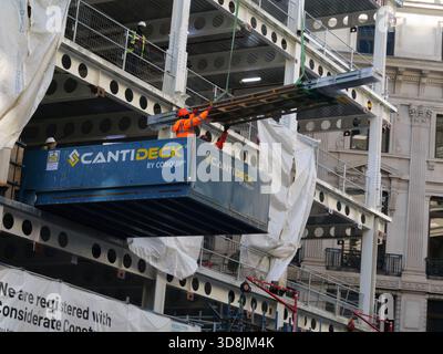 Bauarbeiter fangen Baumaterial, das mit einem Kran geliefert wird, während er auf einem Cantideck steht, einer temporären, auskragenden Kranladeplattform, die auf Baustellen zum Verladen von Materialien in oder aus Hochhäusern verwendet wird Stockfoto