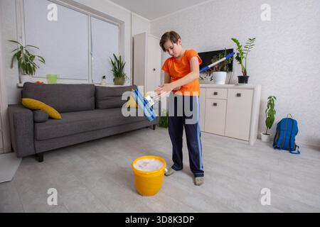 Der Junge reinigt das Wohnzimmer mit einem Mopp. Stockfoto