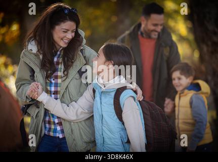Vierköpfige Familie spaziert durch den sonnigen Wald, genießt ihre Wanderung, während sie Wanderstöcke trägt und tagsüber zusammen lächelt Stockfoto