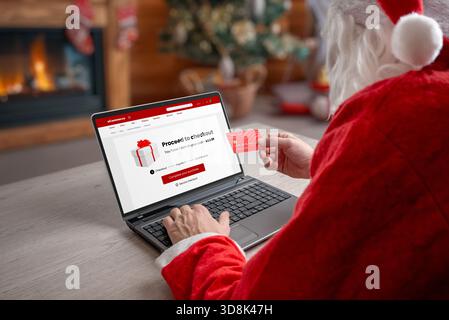 Weihnachtsmann, der die Online-Kasse auf einem Laptop mit Kreditkarte im warmen Weihnachtsinnenraum abschließt, ideal für E-Commerce-Themen, Weihnachtseinkaufaktionen und vieles mehr Stockfoto