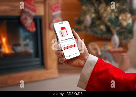 Smartphone mit Weihnachtsmann-Hand und Bildschirm zur Kasse in gemütlichem Weihnachtsinnenraum, ideal für Online-Shopping-Themen, festliches Marketing und E-Comme Stockfoto