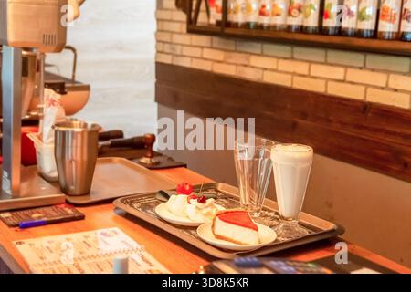 Ein Kellner in einem Café bereitet Milchshake, Käsekuchen und Eis mit Obst zu, um Freunde in einem kleinen Café zu treffen Stockfoto