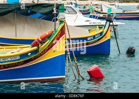 Marsaxlokk, Malta - 13. April 2025: Traditionelle, farbenfrohe maltesische Fischerboote namens Luzzu mit hellblauen, gelben und roten Details, die im malerischen Hafen von Marsaxlokk ankern Stockfoto