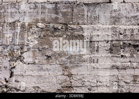 Die verwitterte Steinwand zeigt Risse und raue Texturen, die Alter und Verfall zeigen. Die Umgebung im Freien unterstreicht rustikalen Charme bei hellem Tageslicht. Stockfoto