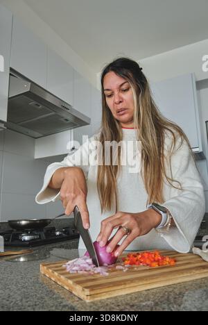 Frau, die sich unangenehm fühlt, während sie eine Zwiebel in einer modernen Küche hackt Stockfoto