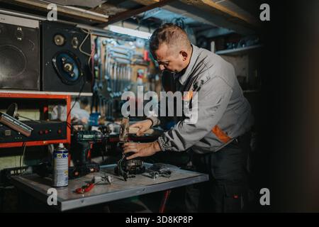 Mechaniker, der in einer übersichtlichen Werkstatt arbeitet und Ausrüstung mit Elektrowerkzeugen und Handwerkzeugen repariert Stockfoto