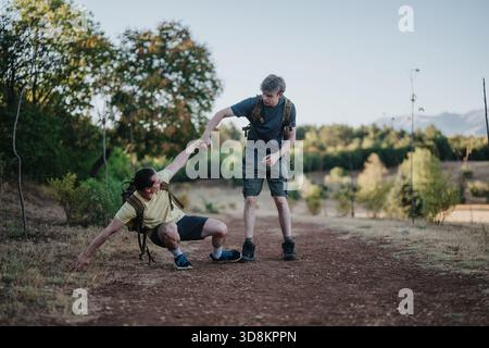 Zwei Wanderer auf einem Feldweg helfen sich bei einer sonnigen Wanderung im Freien Stockfoto