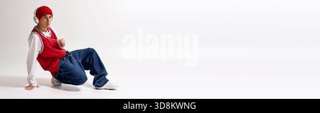 Teen posiert selbstbewusst mit rotem Hut und sackiger Jeans vor weißem Hintergrund, Banner Stockfoto