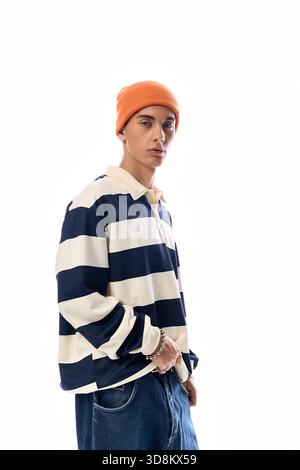 Ein Teenager steht selbstbewusst in einem gestreiften Langarm-Poloshirt und einem orangefarbenen Hut vor weißem Hintergrund. Stockfoto