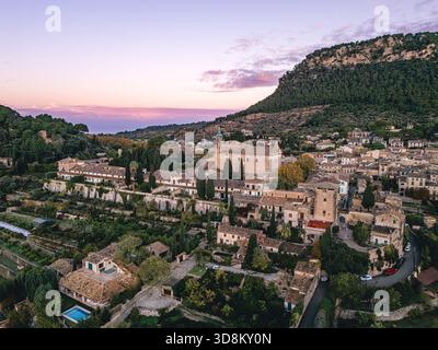 Bei Sonnenaufgang offenbart eine Drohne Valldemossa, eingebettet zwischen Terrassenfeldern und felsigen Hängen, dessen Steingebäude sanft im Morgenlicht leuchten. Stockfoto
