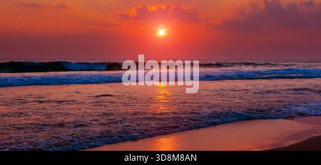 Wunderschöner Sonnenuntergang über Meer oder Meer. Lebendige und weiche Farben, magisches Licht. Kleine Wolken am Himmel, Spiegelung der Sonne im Wasser und Sand am Strand. Stockfoto
