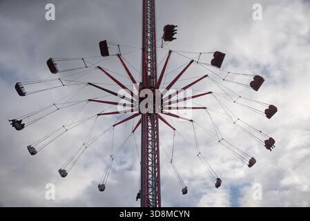 Eine Fahrt mit dem Chair-O-Planes auf dem Messegelände mit einem dramatischen, bewölkten Himmel, der die zentrale Struktur und die Sitze hervorhebt. Stockfoto