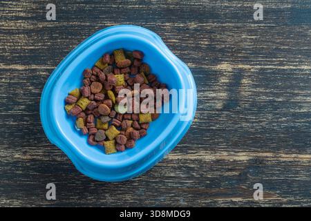 Katze getrocknetes Futter in einer blauen Plastikschale auf Holzhintergrund, Draufsicht, Nahaufnahme, Kopierraum Stockfoto