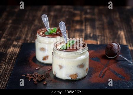 Traditionelles italienisches Dessert Tiramisu dekoriert mit Kakaopulver und grüner Minze im Glas auf dem Tisch, Nahaufnahme Stockfoto