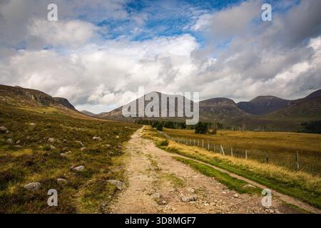 Eine schroffe Feldstraße schlängelt sich durch ein grasbewachsenes Tal in Richtung entfernter Berge unter den dramatischen Mourne Mountains, Nordirland Stockfoto