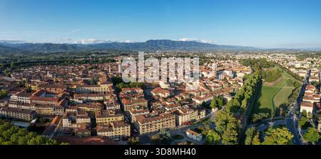 Aus der Vogelperspektive treffen die Terrakotta-Dächer auf smaragdgrüne Parks unter einem riesigen Himmel, eingerahmt von fernen Bergen, Lucca, Toskana, Italien. Stockfoto