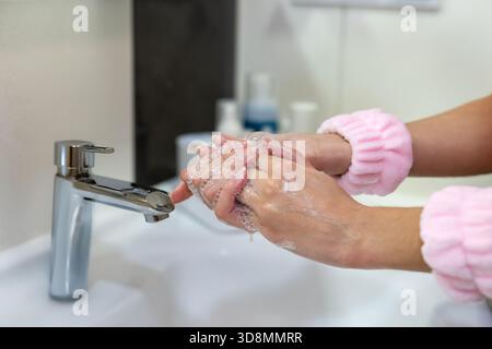Frau wäscht Hände mit Seife im Waschbecken. Nahaufnahme einer Frau, die ihre Hände mit Seife unter fließendem Wasser an einem Waschbecken im Bad aufschäumt, was sie fördert Stockfoto