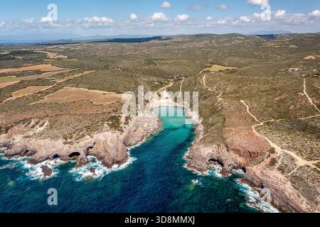 Vogelperspektive auf eine abgelegene Bucht entlang zerklüfteter Klippen, lebendigem türkisfarbenem Wasser und trockenen Hügeln mit gewundenen Pfaden. Ideal für Reisen, Natur, Küste und Stockfoto