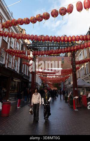 London, Vereinigtes Königreich, 23. November 2025: Menschen, die unter dem traditionellen chinesischen Bogen spazieren, umgeben von Läden und Laternen Stockfoto