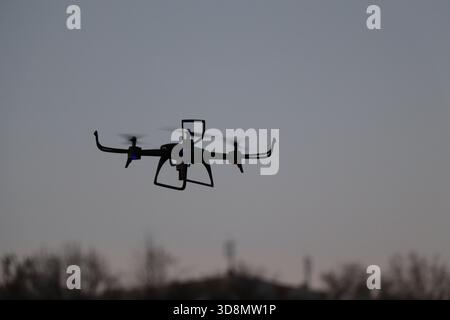 Drohne fliegt bei Sonnenuntergang – Quadcopter-Silhouette im Abendhimmel. Quadcopter Drohne im Flug während der Dämmerung mit Soft Cloud Stockfoto