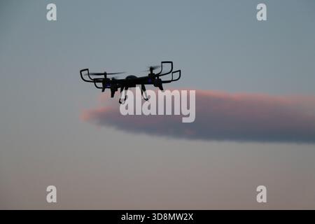 Drohne fliegt bei Sonnenuntergang – Quadcopter-Silhouette im Abendhimmel. Quadcopter Drohne im Flug während der Dämmerung mit Soft Cloud Stockfoto