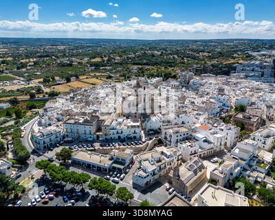 Aus der Vogelperspektive auf ein Meer von weißen Gebäuden, die um eine zentrale Kirche gruppiert sind, die Architektur glitzert unter einem hellen Himmel, Locorotondo, Apulien, Italien. Stockfoto