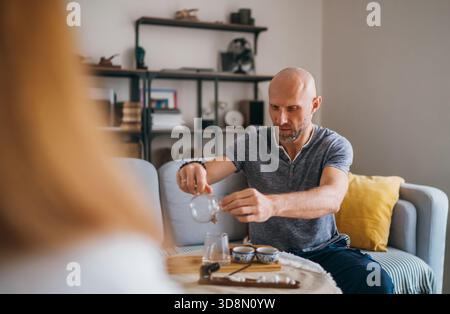Entspanntes Paar trinkt Tee gemütliches Wohnzimmer, das warme Gespräche teilt und einen ruhigen Morgenmoment genießt. Die gemütliche Atmosphäre zu Hause betont die Verbindung Stockfoto