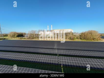 Aus der Vogelperspektive erstrecken sich die Reihen von Solarpaneelen in Richtung Industriebauten unter dem riesigen blauen Himmel, Spalding, England, Vereinigtes Königreich. Stockfoto