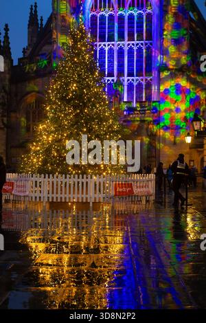 Ein großer, mit Lichtern geschmückter Weihnachtsbaum steht vor einem Gebäude mit farbenfrohen Projektionen. Die Menschen sind im Hintergrund sichtbar, und das wir Stockfoto