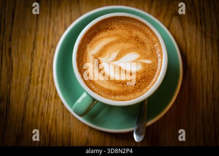 Eine Nahaufnahme von einem Latte mit Latte Art auf einem Holztisch. Stockfoto