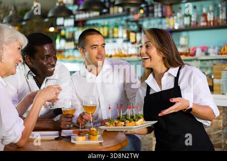 Fröhliche junge Kellnerin brachte Tablett mit Bestellung zu den Pub-Gästen Stockfoto