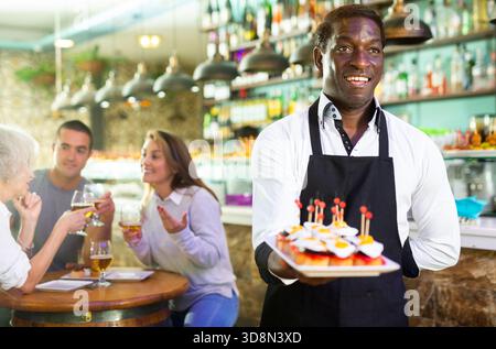 Ein Blick auf den erwachsenen afrikanischen Mann mit Pinchos in einer Bar Stockfoto