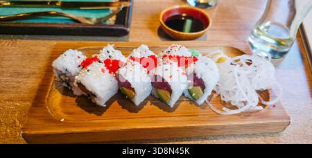 Farbenfrohe Sushi-Brötchen sind wunderschön auf einem Holzteller angeordnet, begleitet von Dip-Sauce und Garnituren, die kulinarische Kunst zeigen. Stockfoto