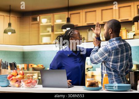 Wütende afroamerikanische Freundin, die ihre Hand hebt, um ihren Partner zu schlagen, aggressives Argument mit häuslicher Gewalt. Eine hysterische Freundin wurde von einem enttäuschten Freund in der Küche angehalten. Stockfoto