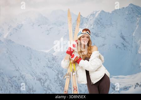 Glücklicher junger Tourist in Winterkleidung mit Holzskier vor verschneiten Bergkulissen, Symbol für Skiwochenende, Verleih und alpine Erholung Stockfoto