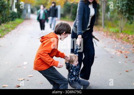 Eine glückliche Familie genießt eine gute gemeinsame Zeit, während Kinder spielerisch auf einem malerischen Waldweg laufen. Lachen erfüllt die Luft zwischen lebhaftem Herbstlaub und einer ruhigen Atmosphäre. Stockfoto