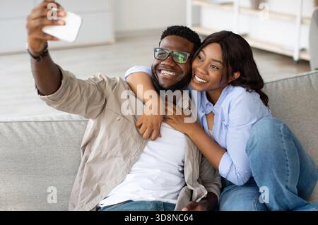 Das glückliche Schwarze Paar genießt einen gemütlichen Moment bei einem Selfie in seinem Wohnzimmer Stockfoto