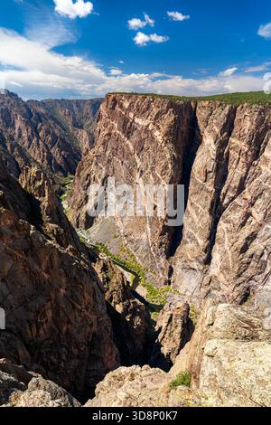 Blick auf die massive Painted Wall im Black Canyon des Gunnison National Park. Weiße Pegmatitdeiche bilden Streifen auf der dunklen, transparenten Klippe. Der Gunnison River ist unten sichtbar Stockfoto