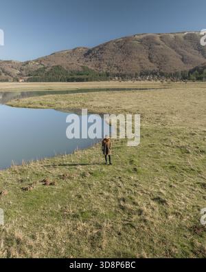 Aus der Vogelperspektive steht am grasbewachsenen Rand eines ruhigen Sees, unter einem weiten Himmel, umgeben von der rauen Bergkulisse Laceno Lake, Irpini Stockfoto