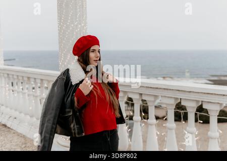Frau Baskenmütze Balkon. Elegante Frau in einer roten Baskenmütze posiert auf einem Balkon am Meer. Stockfoto