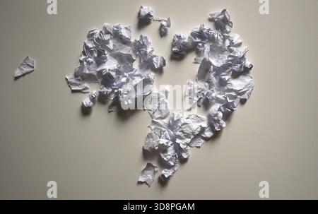 Konzeptuelle Fotografie: Eine zerrissene Herzform aus zerknitterten Papierfragmenten auf einer neutralen Oberfläche. Symbolisiert Zusammenbruch, Beziehungsende, Traurigkeit, Stockfoto