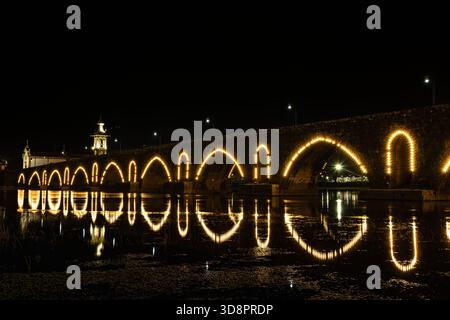 Nächtlicher Blick auf die Brücke Ponte de Lima, die sich auf dem Fluss mit Weihnachtslichtern spiegelt - Portugal Stockfoto