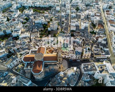 Aus der Vogelperspektive auf weiß getünchte Gebäude, die eng um eine Kirche mit einem hohen Glockenturm gruppiert sind und ein Labyrinth aus Texturen und Tönen schaffen, Alberobello, Apu Stockfoto