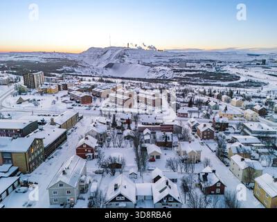 Aus der Vogelperspektive auf eine schneebedeckte Stadt, die unter der Eisenerzmine liegt, während die Polarnacht den Himmel in zarten Tönen färbt: Kiruna, Norrbotten Coun Stockfoto